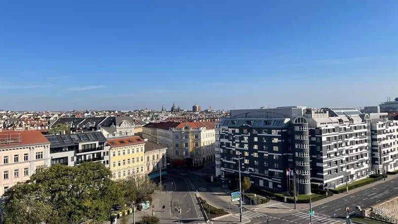 Panoramablick über eine Stadt mit historischen Gebäuden und modernen Strukturen unter klarem blauem Himmel.