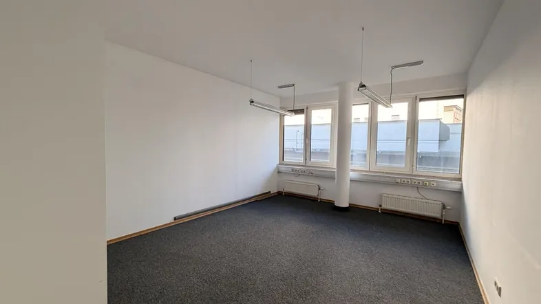Helles, leeres Büro mit Teppichboden und großen Fenstern, ideal für neue Mieter.