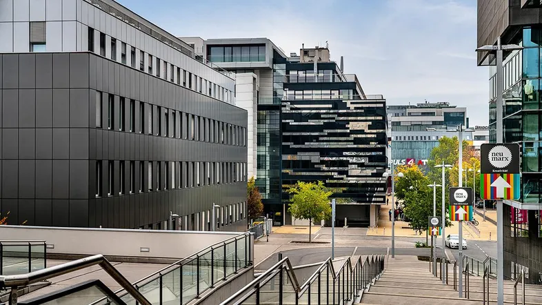 Moderne Bürogebäude mit Glasfassaden und einer breiten Treppe, die zu einem städtischen Platz führt.