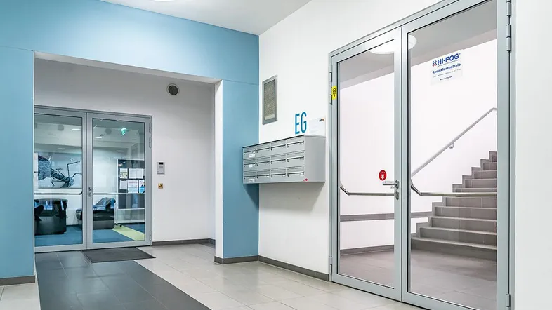 Heller Eingangsbereich mit Briefkästen, Treppenhauszugang und Zugang zu weiteren Räumen in einem modernen Gebäude.
