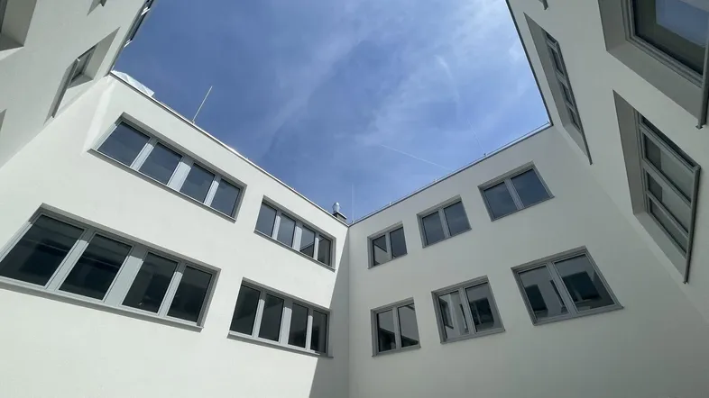 Blick in den Innenhof eines modernen Gebäudes mit vielen Fenstern und hellem Himmel.