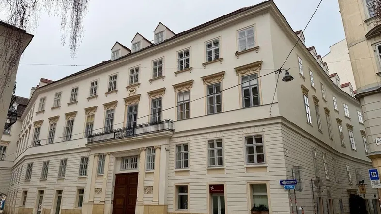 Klassisches Gebäude mit mehreren Stockwerken und traditioneller Architektur an einer gepflasterten Straße in der Stadt.