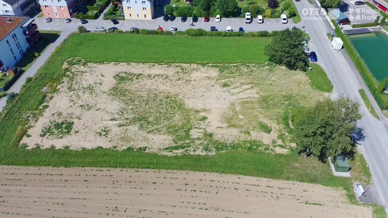 Luftaufnahme eines großen Baugrundstücks, umgeben von Grünflächen und Wohngebäuden in der Ferne.