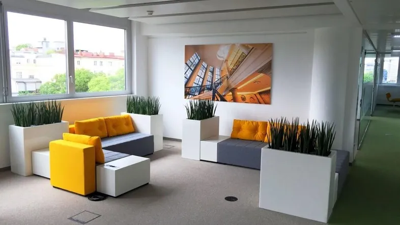 Moderner Loungebereich mit bequemen Sitzgelegenheiten in Grau und Gelb sowie großen Fenstern.