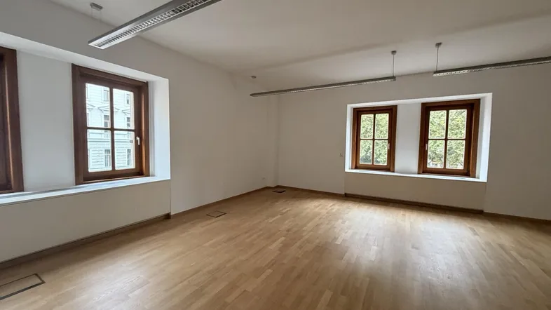 Geräumiges Büro mit hellem Holzparkett und großen Fenstern, die viel Tageslicht hereinlassen.