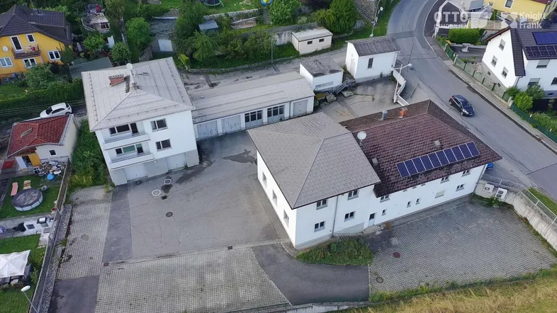 Luftaufnahme eines Anwesens mit mehreren Gebäuden, großzügigen Parkflächen und angrenzender Wohnbebauung.