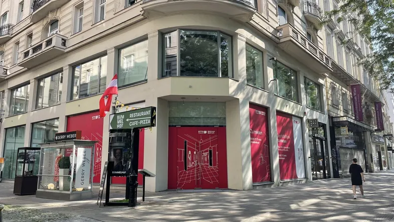 Gebäudeecke mit großen Schaufenstern und roten "Zu vermieten"-Schildern an einer belebten Straße.
