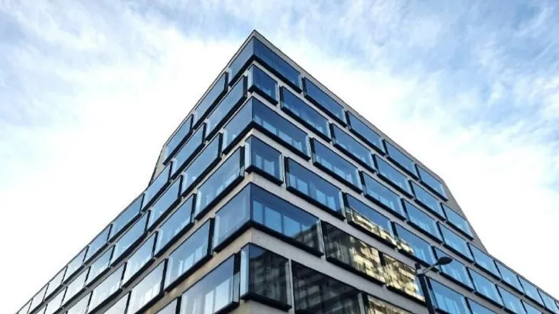 Moderne Bürogebäude-Fassade mit vielen Glasfenstern und einem klaren Himmel im Hintergrund, die eine zeitgenössische Architektur zeigt.