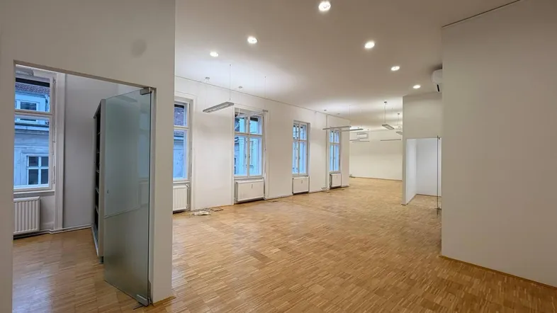 Großer, heller Büroraum mit Parkettboden, vielen Fenstern und moderner Beleuchtung, ideal für flexible Arbeitsbereiche.