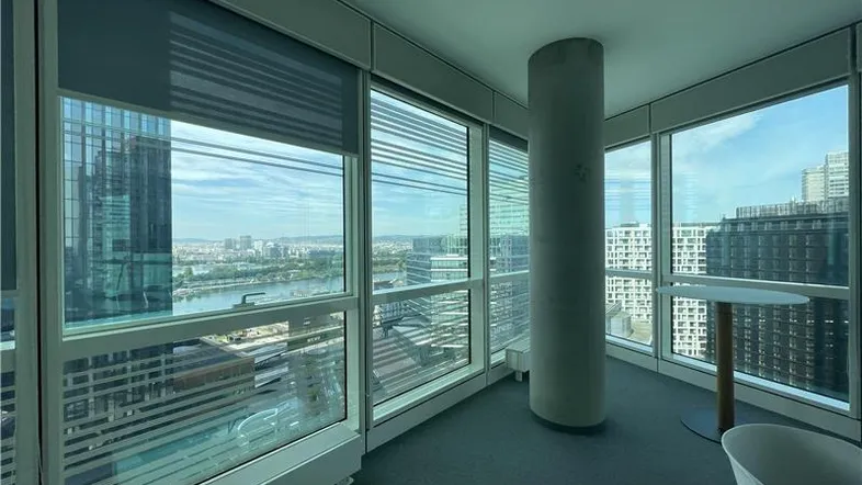 Heller Büroraum mit Teppichboden und raumhohen Fenstern, die einen weiten Stadt- und Flussblick bieten.