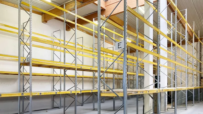 Geräumige Lagerhalle mit hohen Regalsystemen, Betonboden und natürlichem Lichteinfall durch Oberlichter.