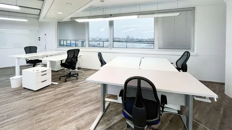 Helles und modernes Büro mit mehreren Arbeitsplätzen, großen Fenstern und Holzboden.