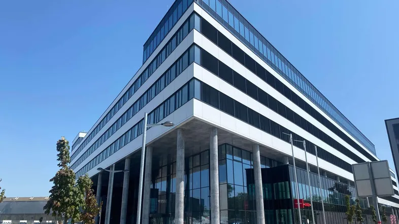 Modernes Bürogebäude mit Glasfassade und klaren Linien unter blauem Himmel.