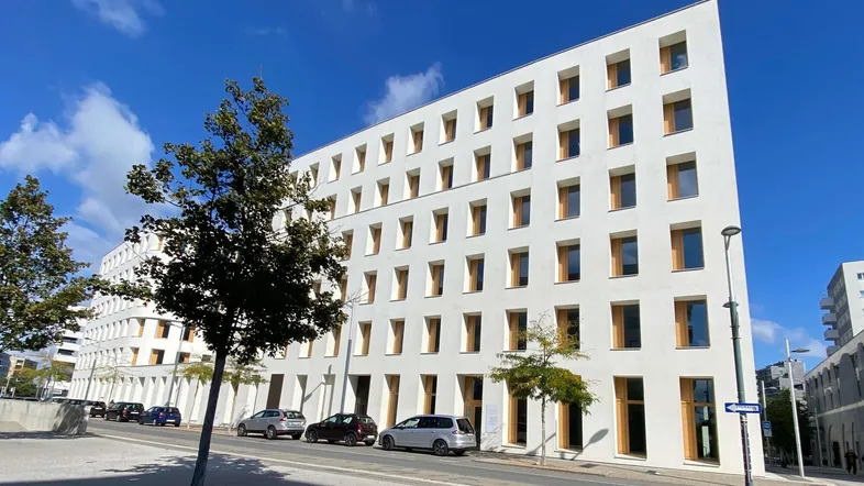 Modernes weißes Gebäude mit vielen Fenstern und klaren Linien an einer städtischen Straße.