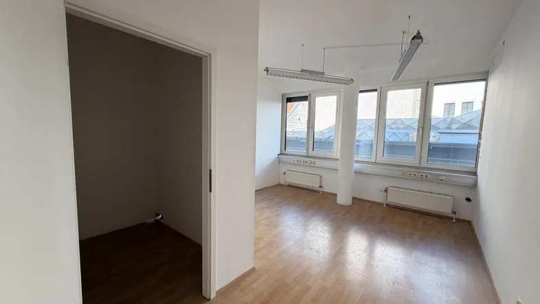 Helles, leeres Büro mit Holzfußboden und großen Fenstern, das viel Tageslicht hereinlässt.