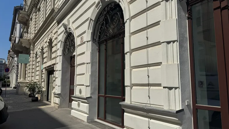 Historische Fassade eines eleganten Gebäudes mit großen Bogenfenstern und dekorativen Elementen an einem sonnigen Tag.