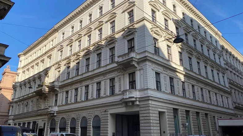 Großes Eckgebäude mit klassischer Architektur, vielen Fenstern und geparkten Autos auf der Straße.