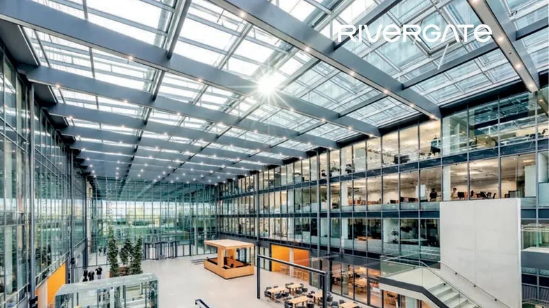 Großzügiges, lichtdurchflutetes Atrium mit Glasdach, modernen Sitzbereichen und Empfangstheke in einem Bürogebäude.