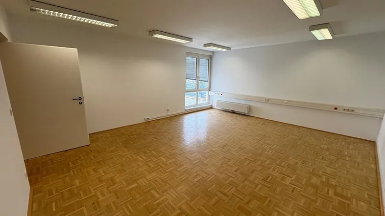 Geräumiges Büro mit hellem Parkettboden, großen Fenstern und viel Tageslicht, ideal für produktives Arbeiten.