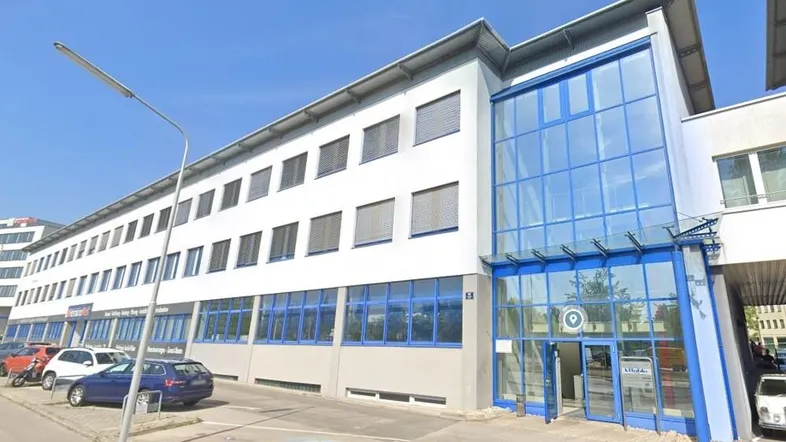 Modernes Bürogebäude mit großer Glasfassade und blauen Akzenten an einem sonnigen Tag.