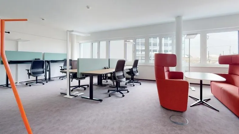 Moderner Büroraum mit ergonomischen Arbeitsplätzen, Teppichboden und bequemen Sitzgelegenheiten für Pausen.