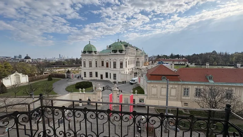 Blick von einem Balkon mit schmiedeeisernem Geländer auf ein historisches Gebäude und die umliegende Stadtlandschaft.