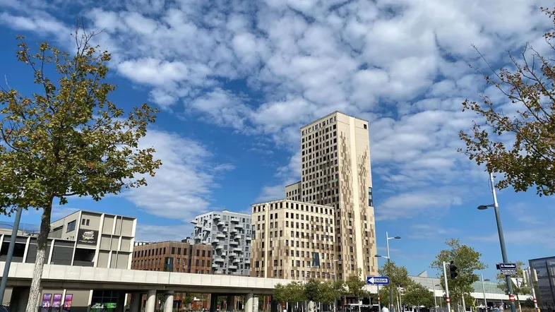 Moderne Hochhäuser und Gebäude in einer städtischen Umgebung unter blauem Himmel mit Wolken.