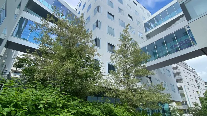 Moderne Gebäude mit hellen Fassaden, verbunden durch gläserne Übergänge und umgeben von üppigem Grün.