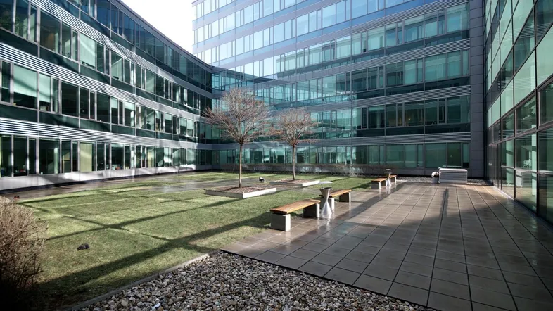 Innenhof eines modernen Bürokomplexes mit Grünflächen, Sitzbänken und gepflasterten Wegen.
