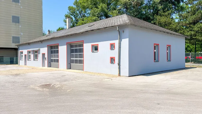 Außenansicht eines Gewerbegebäudes mit mehreren Garagentoren, einer gepflasterten Zufahrt und umgebenden Bäumen.