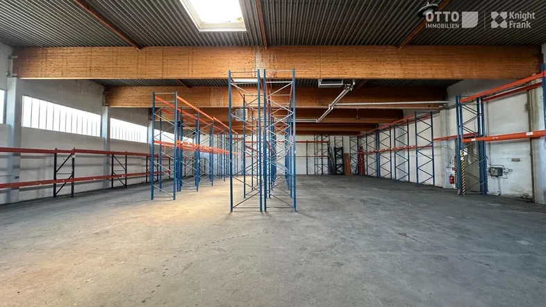 Geräumige Lagerhalle mit hohen Decken, Betonboden und Metallregalen, gut beleuchtet durch Oberlichter.