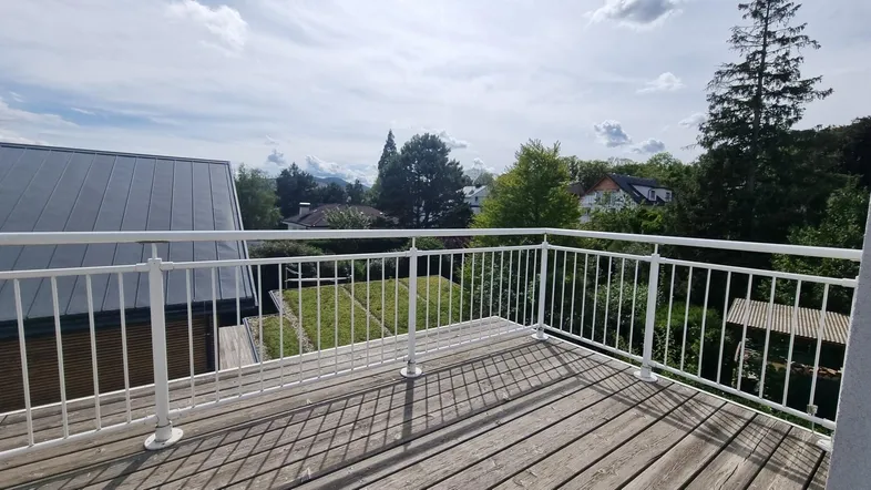 Geräumiger Balkon mit Holzboden und weißem Geländer, bietet einen weiten Blick ins Grüne.