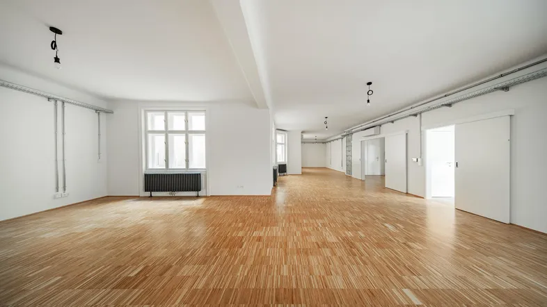 Helles, weitläufiges Zimmer mit Parkettboden und großen Fenstern, ideal für offenes Wohnen.