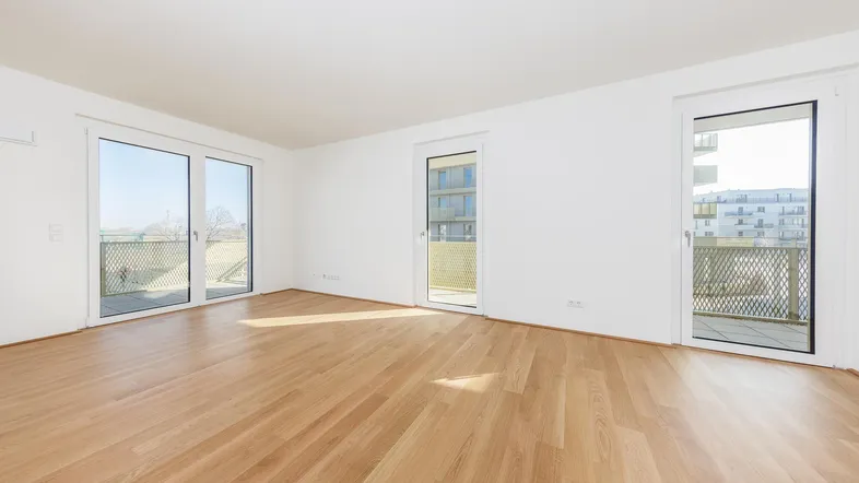 Helles, leeres Zimmer mit Parkettboden und Zugang zu mehreren Balkonen, ideal für individuelle Gestaltung.