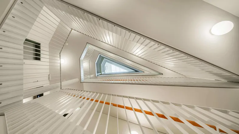 Modernes Treppenhaus mit dreieckiger Öffnung und weißen Geländern, das viel natürliches Licht hereinlässt.