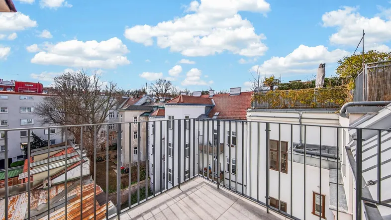 Geräumiger Balkon mit Blick über die Dächer der Stadt und blauem Himmel.