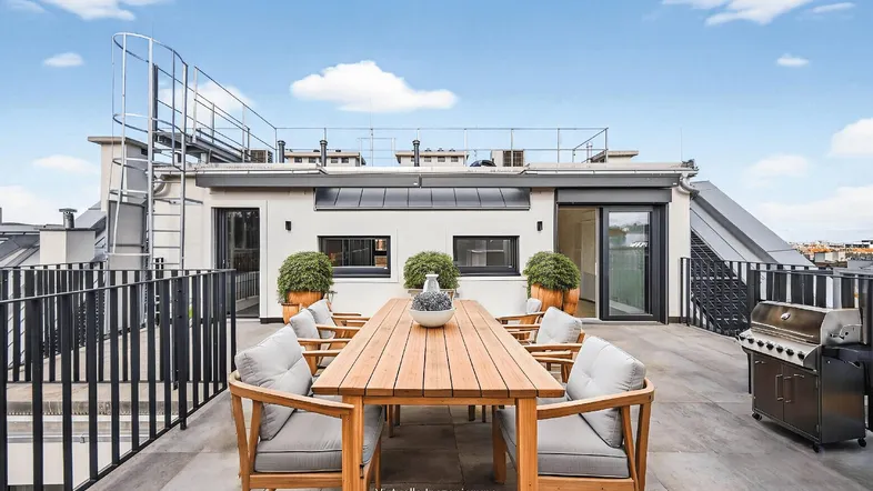 Große Dachterrasse mit Holztisch, Sitzgelegenheiten und Grillbereich, ideal für Mahlzeiten im Freien.