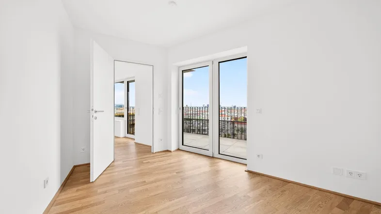 Helles Zimmer mit Holzboden und Zugang zu einem Balkon mit Stadtblick.