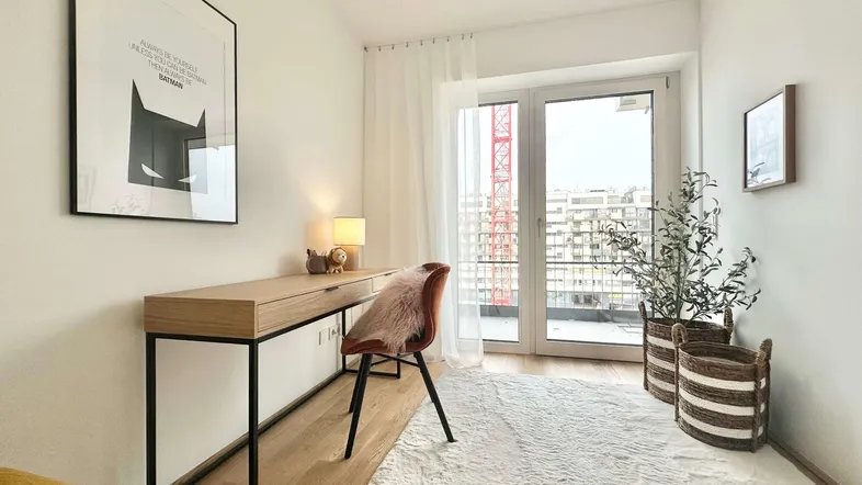 Helles Zimmer mit Schreibtisch, Teppich und Zugang zum Balkon, ideal als Arbeits- oder Gästezimmer.