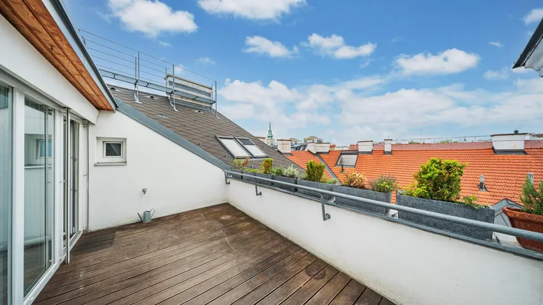 Geräumige Dachterrasse mit Holzboden, Metallgeländer und weitem Blick über die Dächer der Stadt.