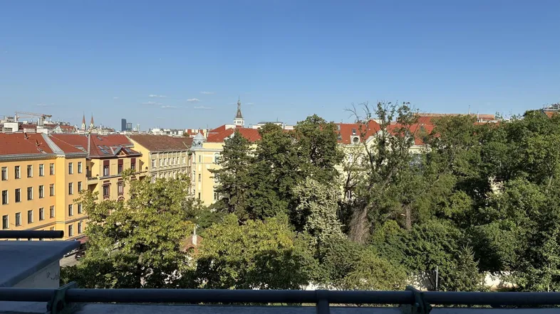 Stadtansicht mit grünen Bäumen und Gebäuden unter blauem Himmel.
