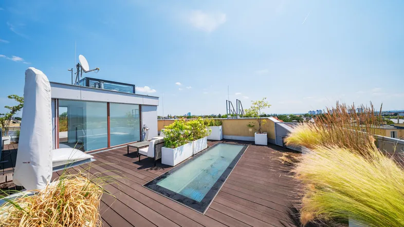 Geräumige Dachterrasse mit Holzbelag, Pflanzen und Blick über die Stadt.