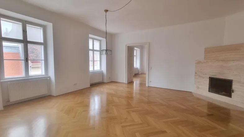 Helles Wohnzimmer mit Fischgrätparkett, hohen Fenstern und einem dekorativen Kamin.