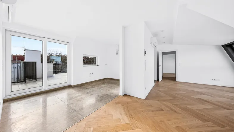 Heller Innenraum mit Parkettboden und Zugang zu einem Balkon, der viel Tageslicht hereinlässt.