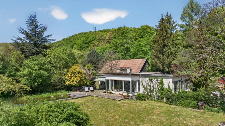 Freistehendes Haus mit großem Garten und umgebender Hügellandschaft unter blauem Himmel.