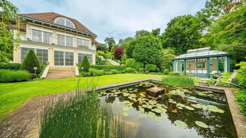 Großer gepflegter Garten mit Zierteich, weitläufiger Rasenfläche und einem eleganten Wintergarten.