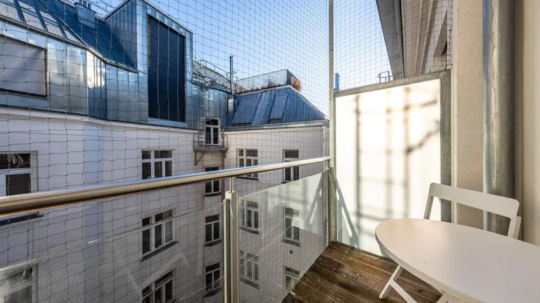 Kleiner Balkon mit Holzboden, Glasbrüstung und Blick auf umliegende Gebäude.
