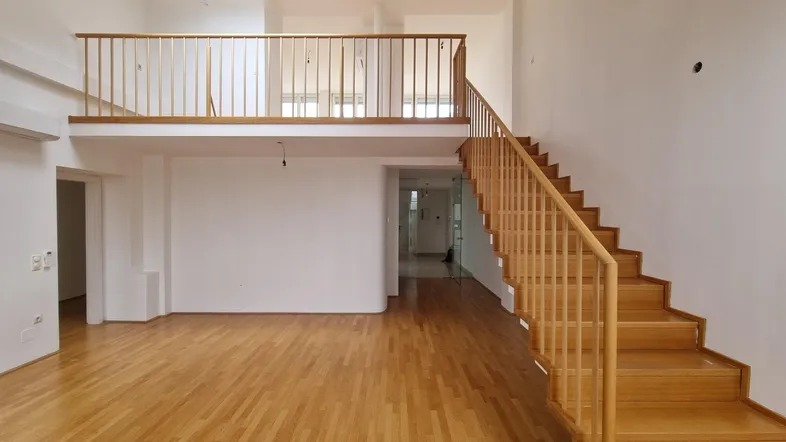 Geräumiger Wohnbereich mit Holztreppe, Galerie und hellem Parkettboden in einem Maisonette-Apartment.