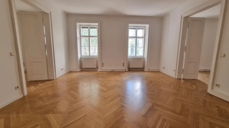 Helles Wohnzimmer mit Fischgrätparkettboden und hohen Flügeltüren, das viel Tageslicht hereinlässt.