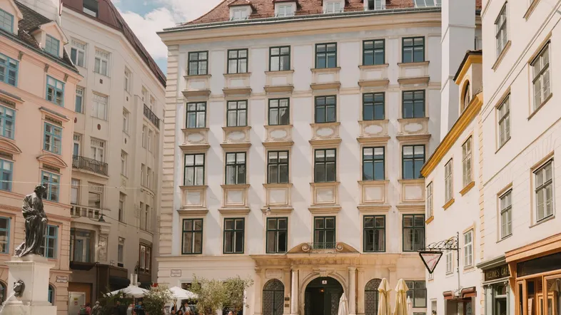 Historisches Gebäude an einem belebten Stadtplatz mit Außengastronomie und klassischer Architektur.